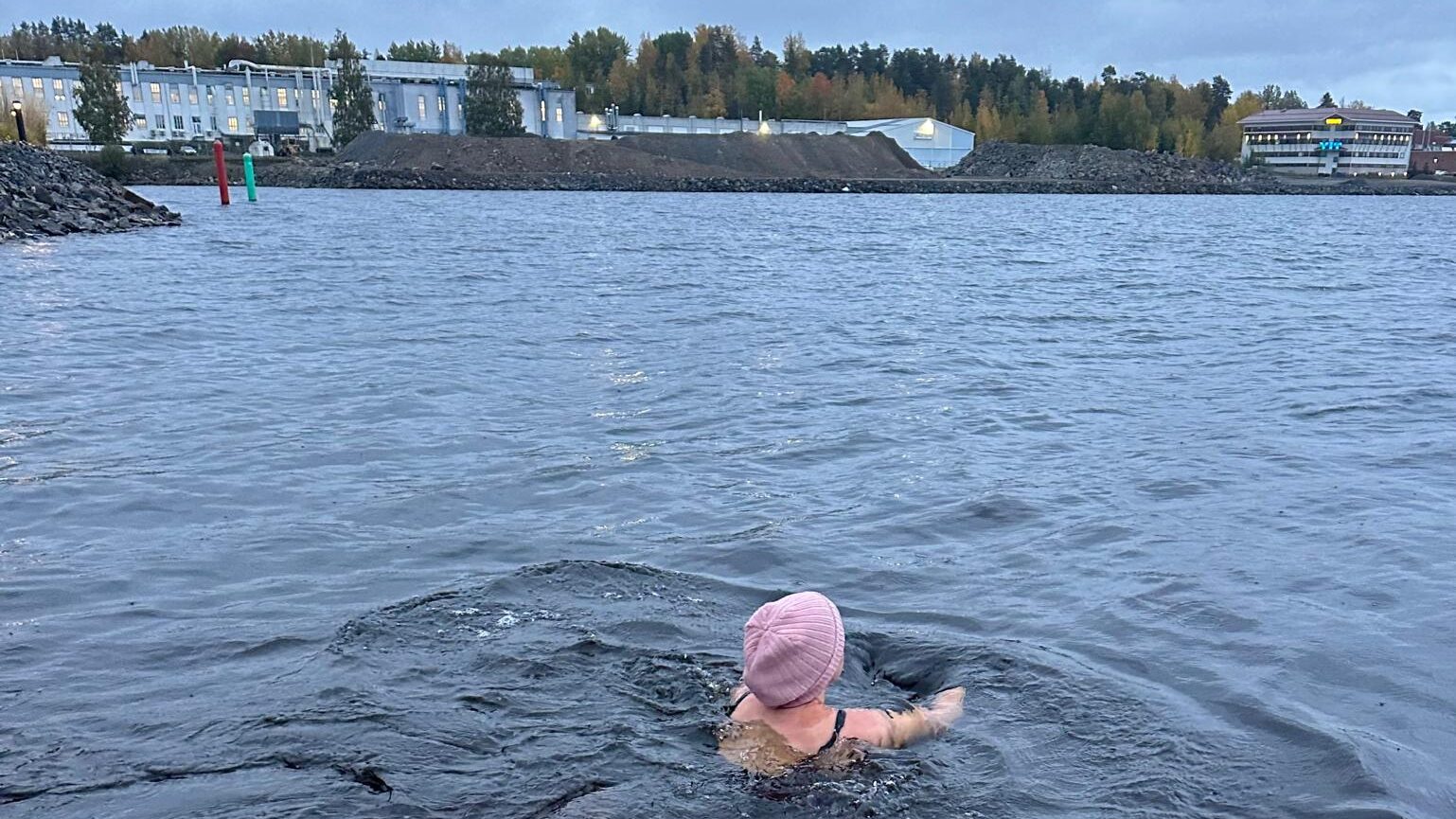 Avantouintia, jossa nainen uimassa myssy päässä kylmässä vedessä, taustalla metsäinen ranta.